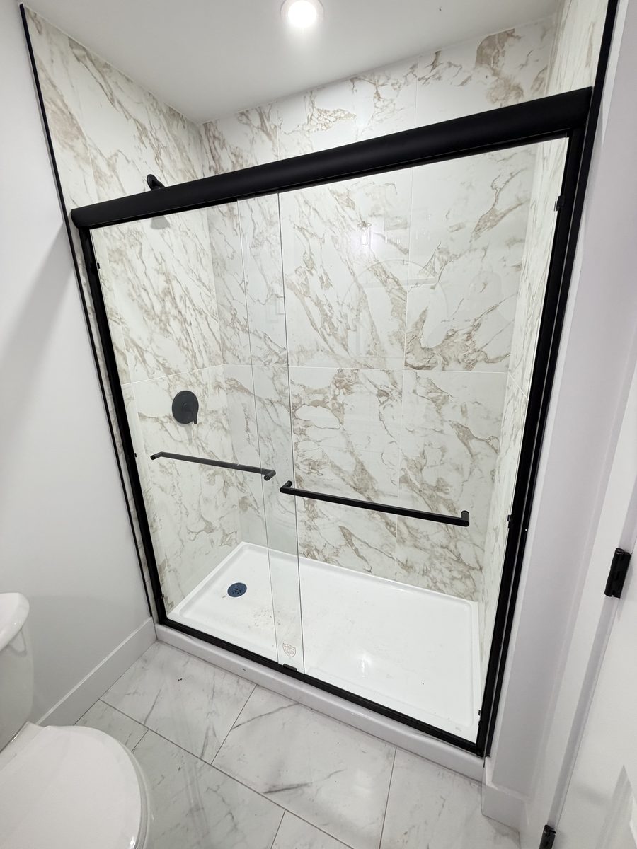 A shower with a black-frame sliding glass door, by High-5 Renovations