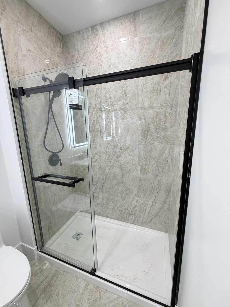 A tiled shower with a black-frame sliding glass door, by High-5 Renovations